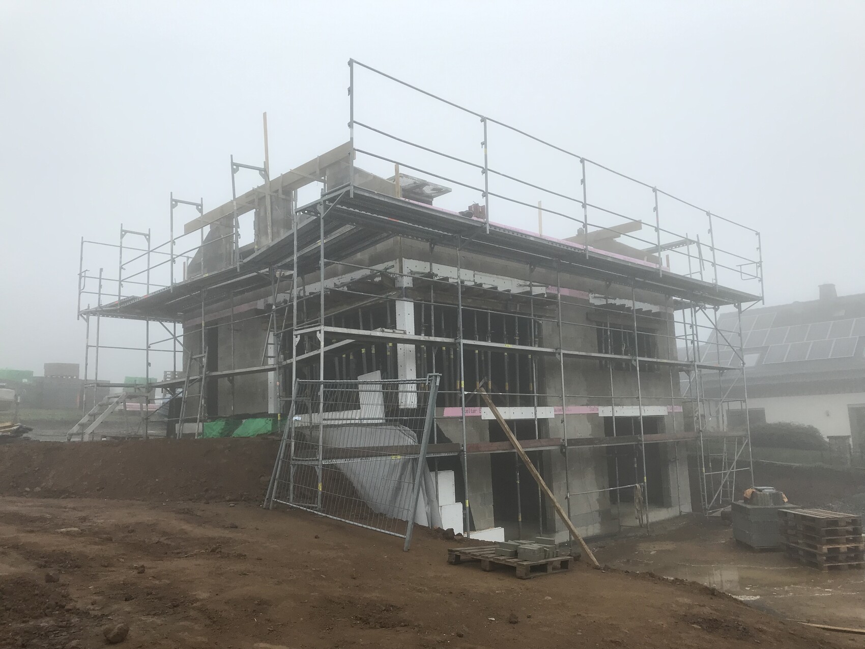 Rohbau eines Gebäudes mit umfangreichem Gerüst, Nebel und Bauzubehör auf einer Baustelle.