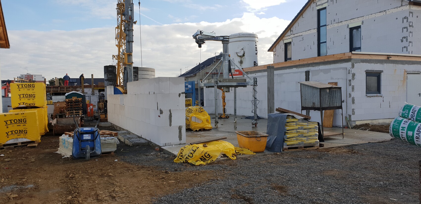 Baustelle mit weißen Betonblöcken, gelben YTONG-Verpackungen, Kran und Baugeräten im Rohbau.