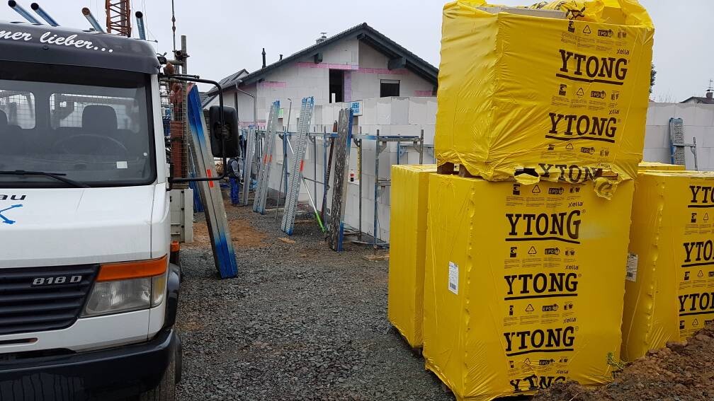 Baustelle: Weißer Lieferwagen links, gelbe YTONG-Verpackungen rechts, Baugerüste dahinter.