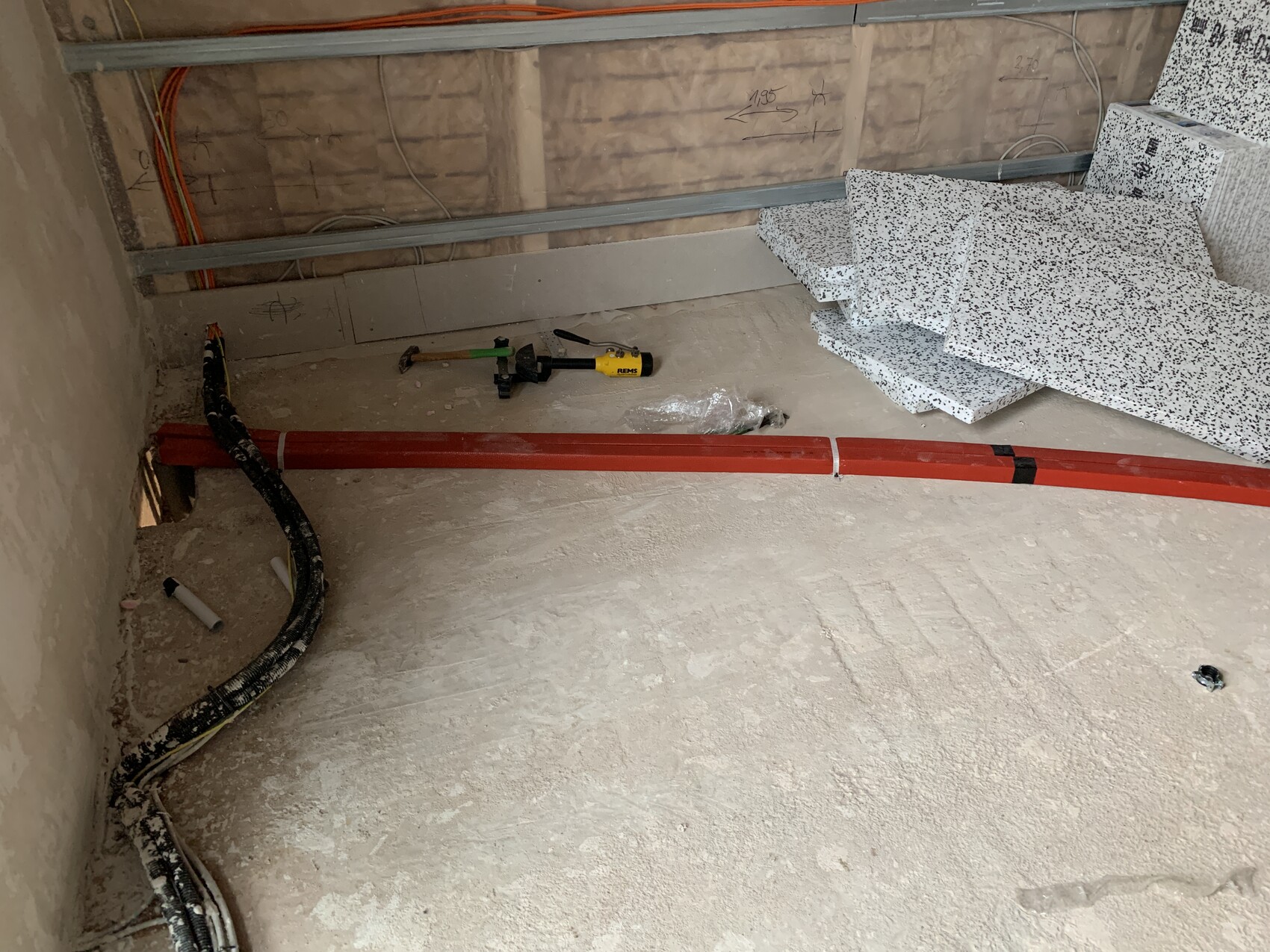 Baustelle: rotes Rohr über staubigem Boden, Kabel, Werkzeuge und gestapelte Platten.