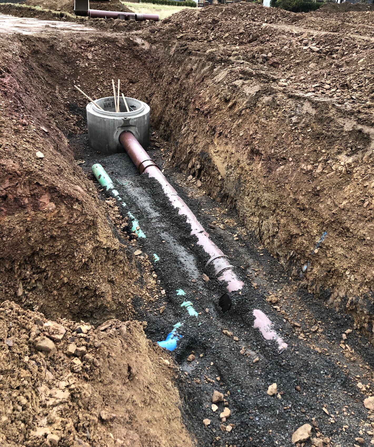 Baugrube mit pinkem PVC-Rohr rundem Betonkanal und Holzstiften im Kies.