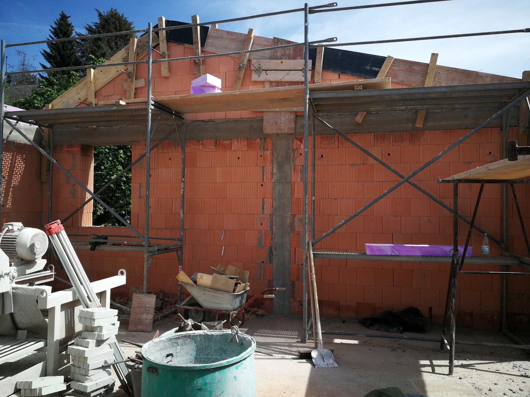 Baustelle: rote Ziegelwand, Stahlgerüst, Bauholz, Schubkarren, Betonmischer, Werkzeug.