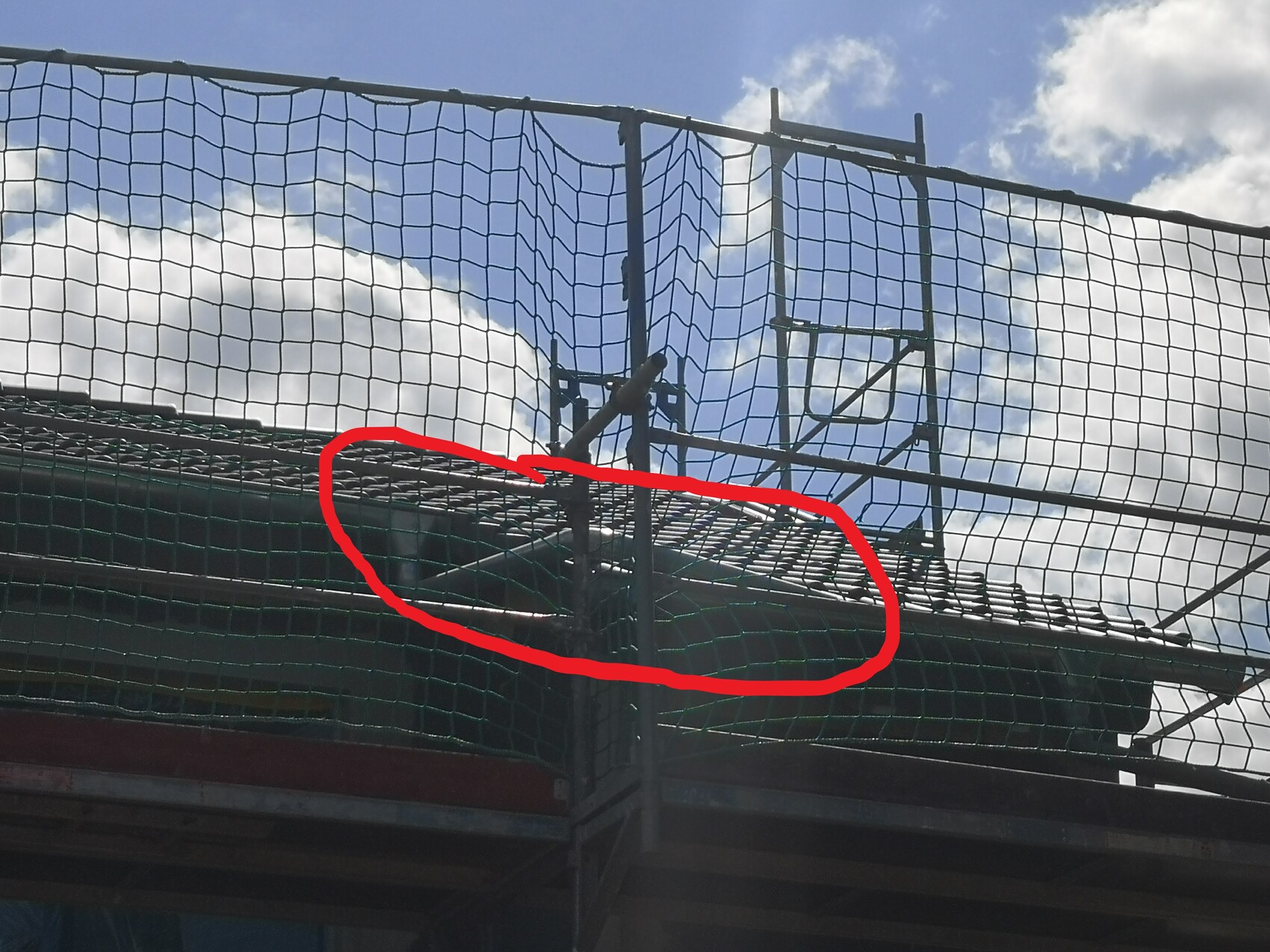 Schutznetz über Baugerüst an einer Dachkante mit Ziegeln, blauer Himmel im Hintergrund