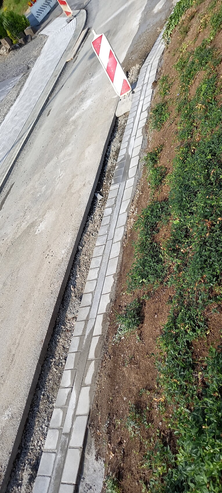 Straßenbaustelle mit rotem und weißem Absperrzeichen, daneben gepflasterter Gehweg und Grünfläche