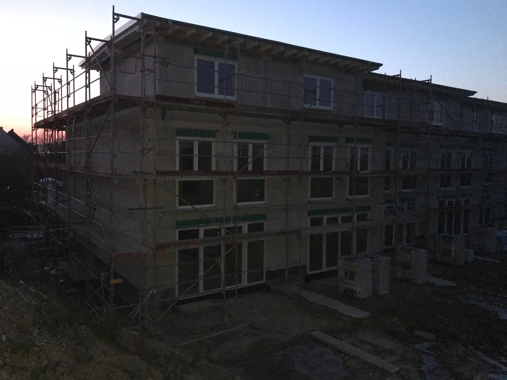 Mehrgeschossiges Gebäude im Rohbau mit Gerüst und Baumaterialien auf einer Baustelle bei Dämmerung