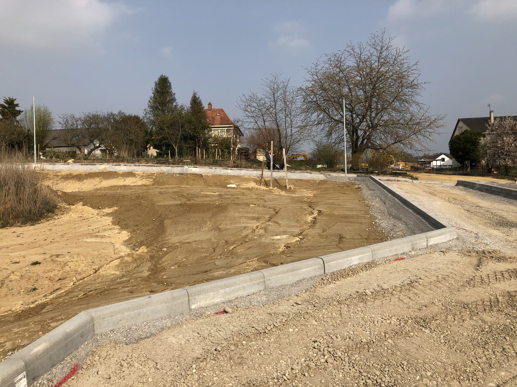 Baustelle: unbefestigte Erdflächen, Bordsteine, Straßenbau, Häuser im Hintergrund.