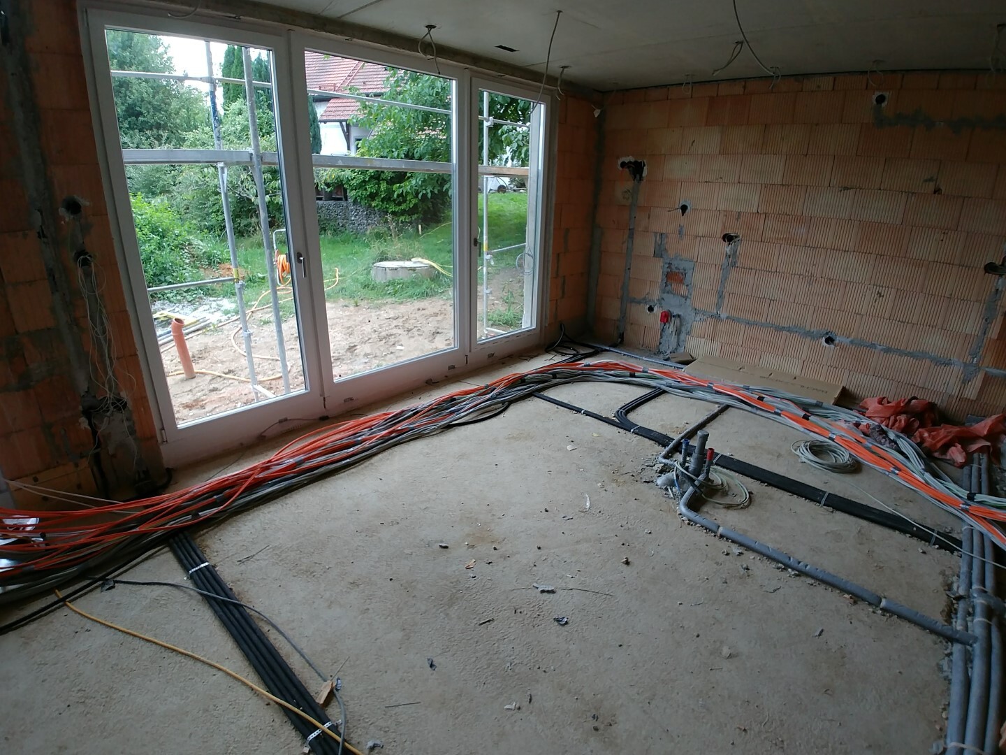 Baustelle im Wohnzimmer mit sichtbarer Elektrikverkabelung, Rohbauwänden und großen Fenstern