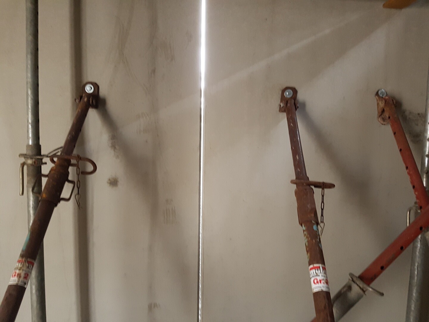 Rostige Baugerüststangen mit Stützen an einer Wand auf einer Baustelle