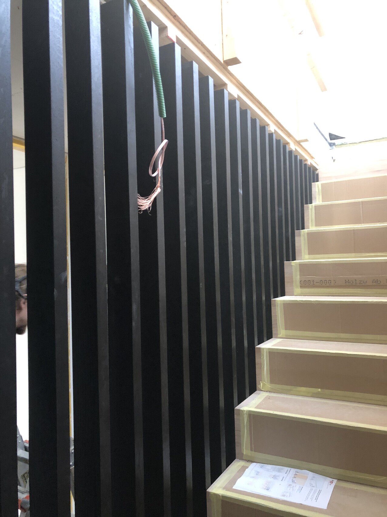 Treppe im Bau: Schwarze Geländerstäbe links, beige Stufen rechts, lose Kabel hängen.