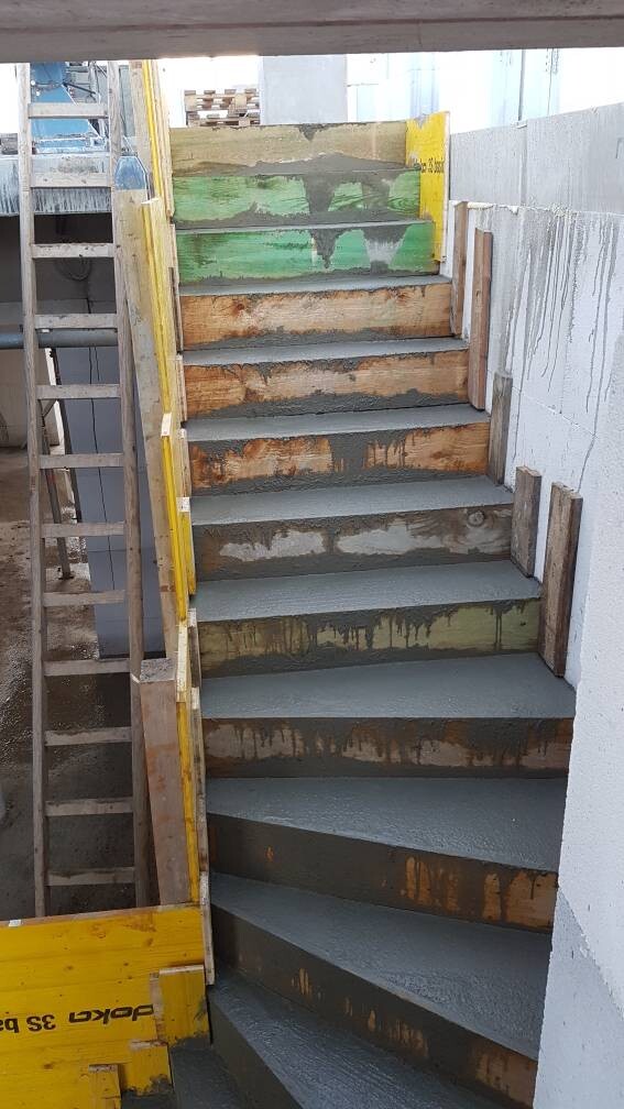 Baustellen-Treppe aus Beton mit Holzformen, feuchter Beton auf Stufen, Geländer in Gelb