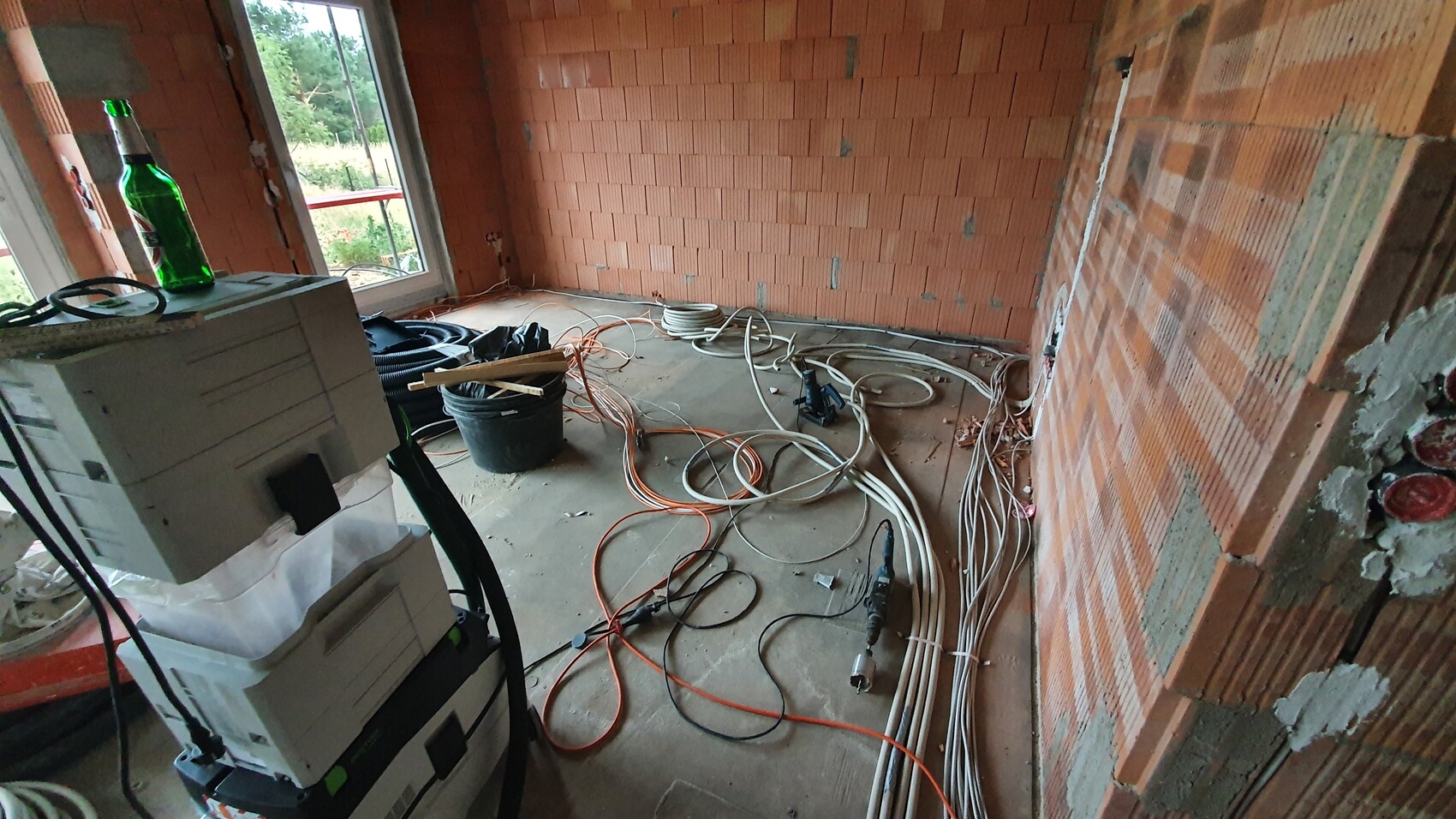 Rohbauzimmer mit offenen Backsteinwänden, Kabelsalat, Werkzeugen und grüner Flasche auf dem Schrank