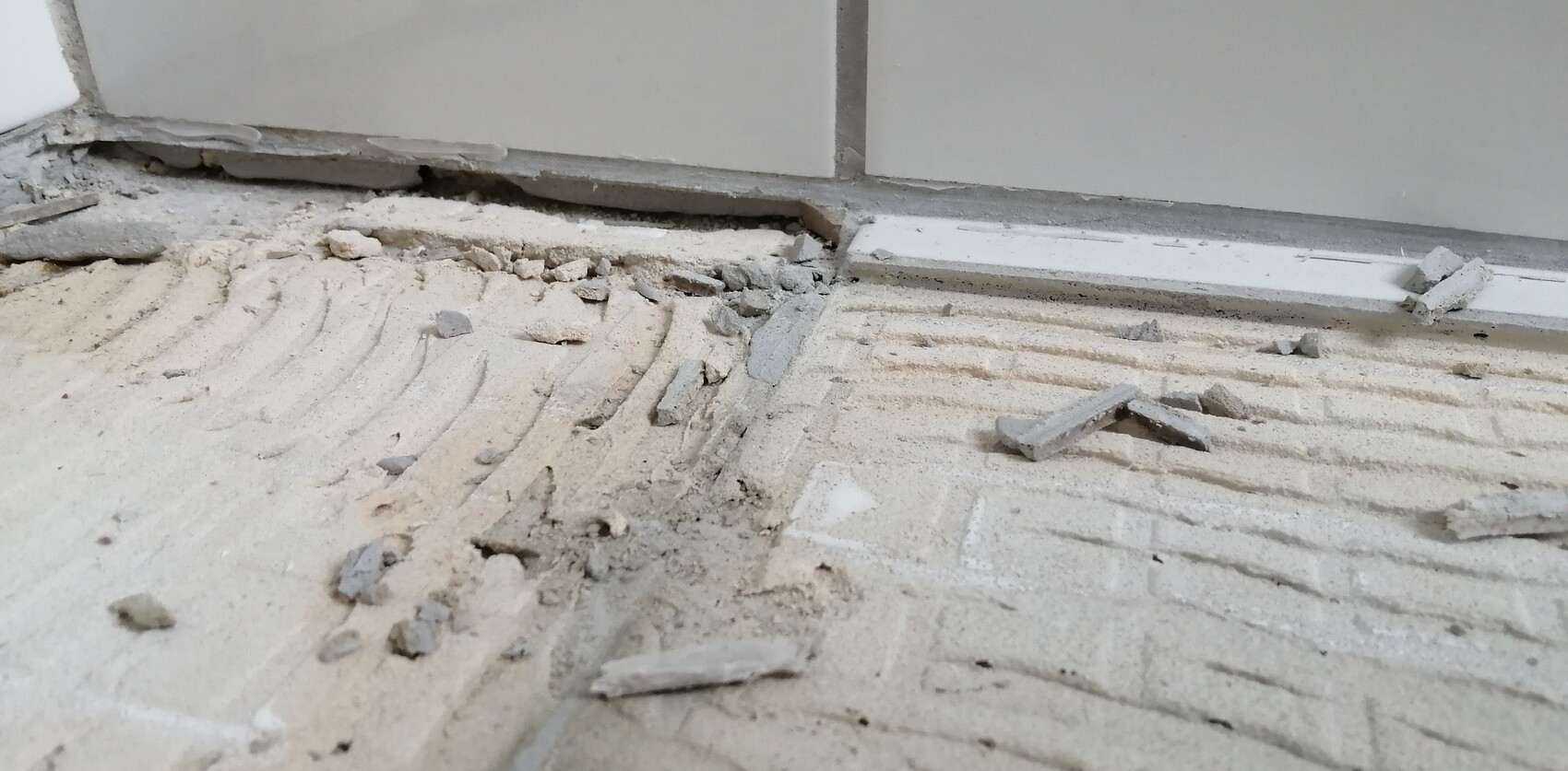 Bodenrenovierung: zerbrochene Fliesenreste, Staub und Trümmer liegen am Boden nahe der Wand.