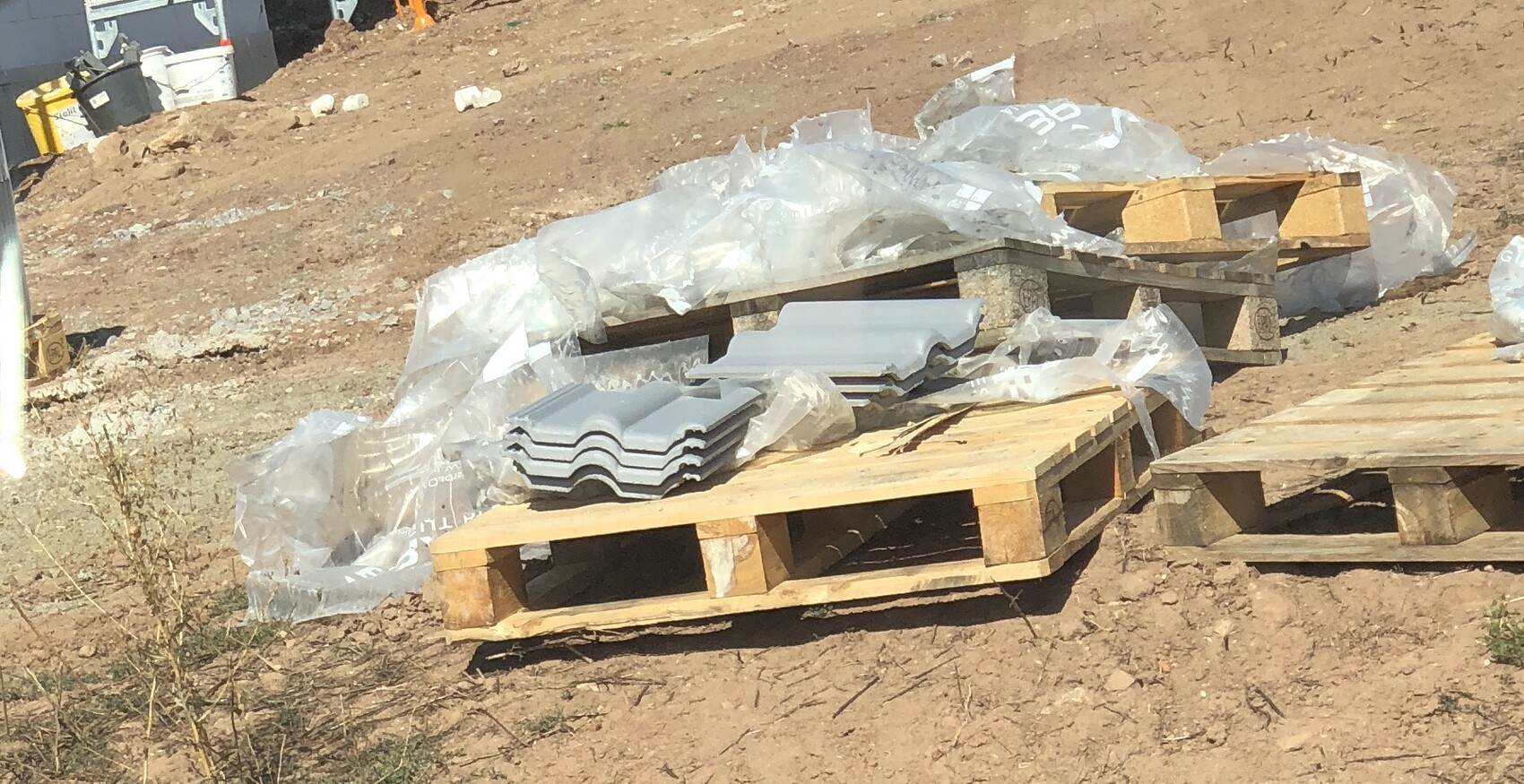 Baustelle mit Paletten grauen Dachziegeln, Plastikfolien und Baumaterialien