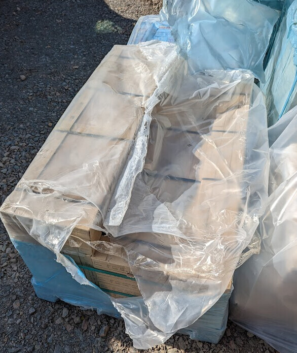 Kartons auf Paletten, verpackt in transparenter Folie, im Außenbereich auf Kies.