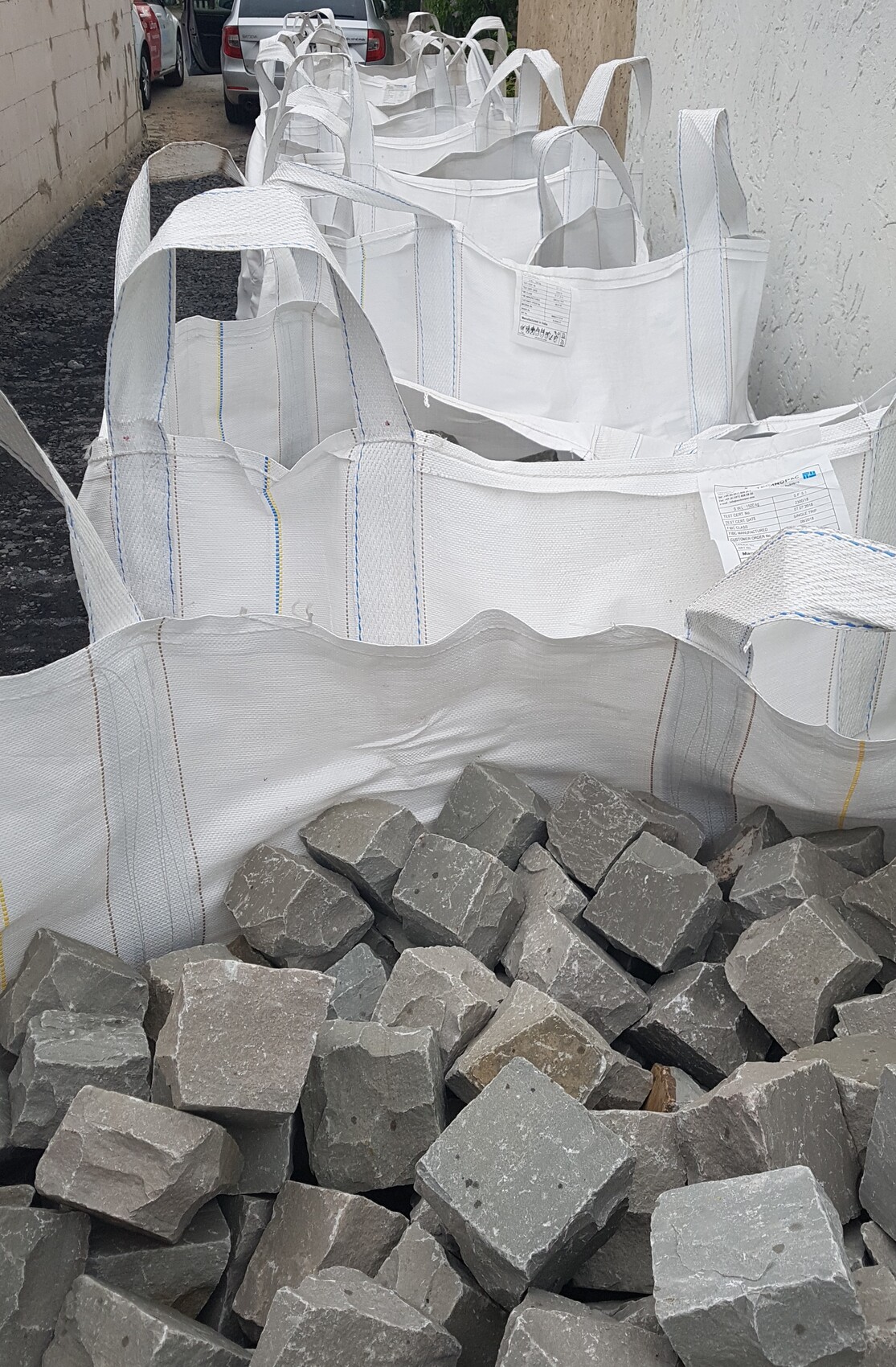 Mehrere große weißen FIBC-Säcke neben einem Haufen grauer Steine in einer Gasse.