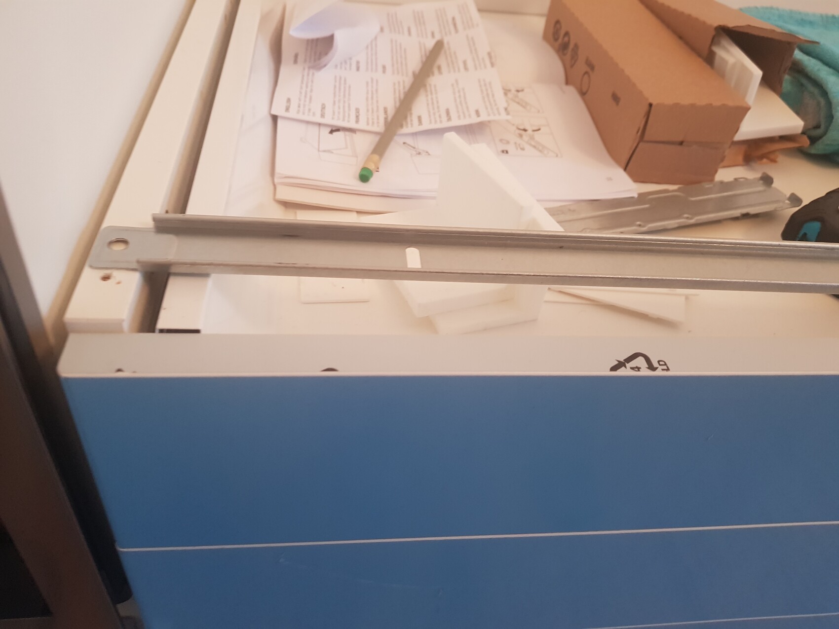 Blaue Schublade mit Metallführung, verstreute Papierstapel, Kartonbox und Werkstattmaterial.