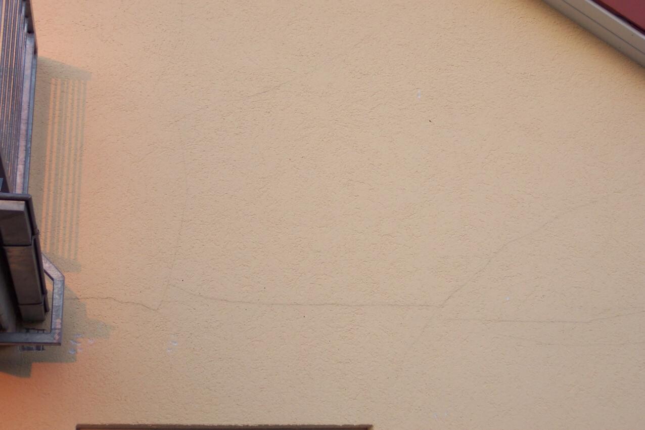 Beige verputzte Außenwand mit Struktur, Gebäudeecke und sichtbarem Bauteil