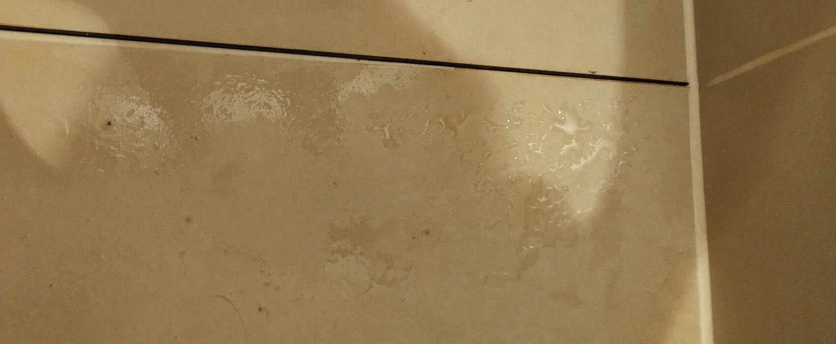 Beige Fliesenboden mit unregelmäßigen, feuchten Flecken.