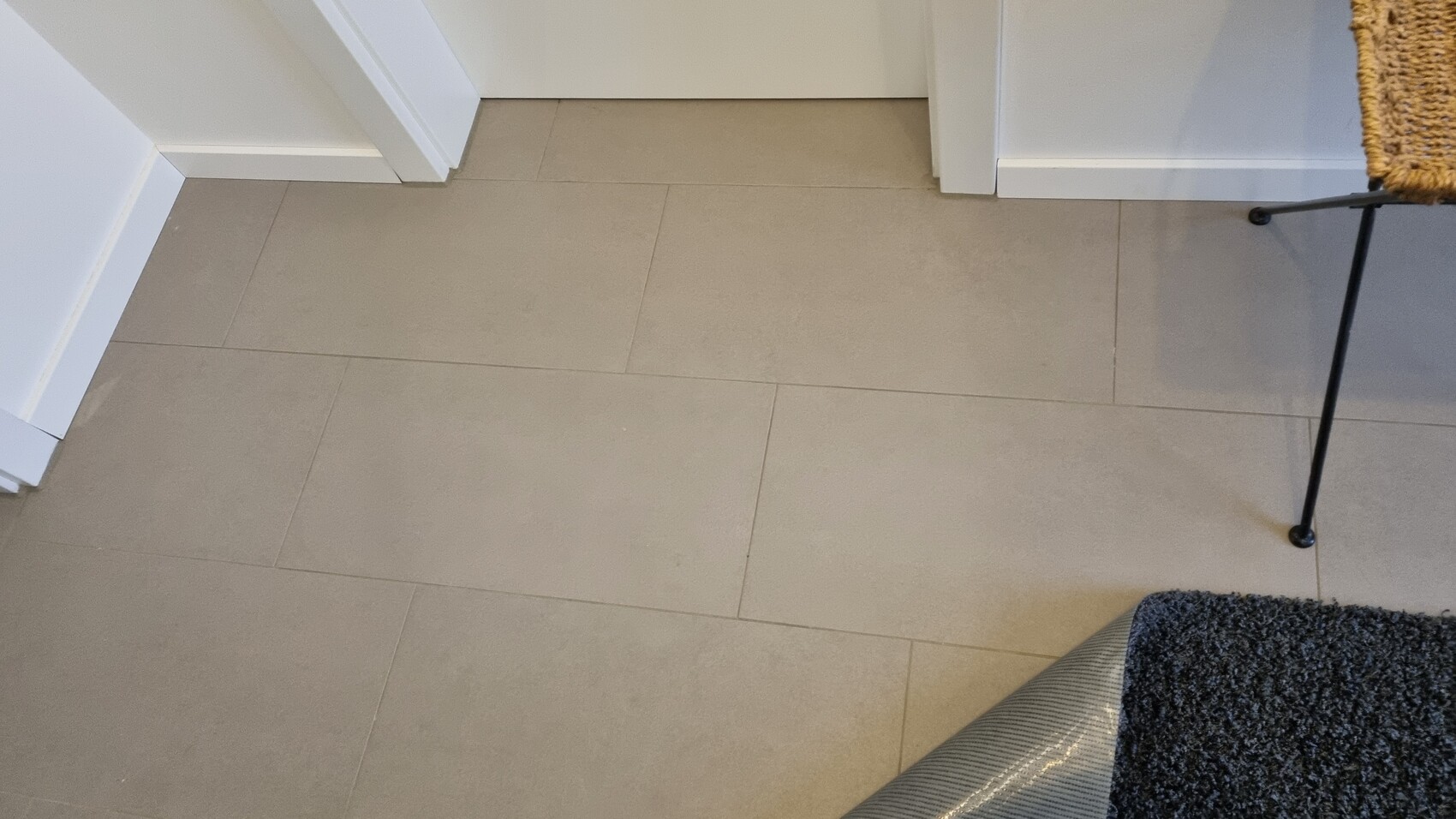 Beige Fliesenboden im Flur mit Türrahmen und Teppichkante sichtbar