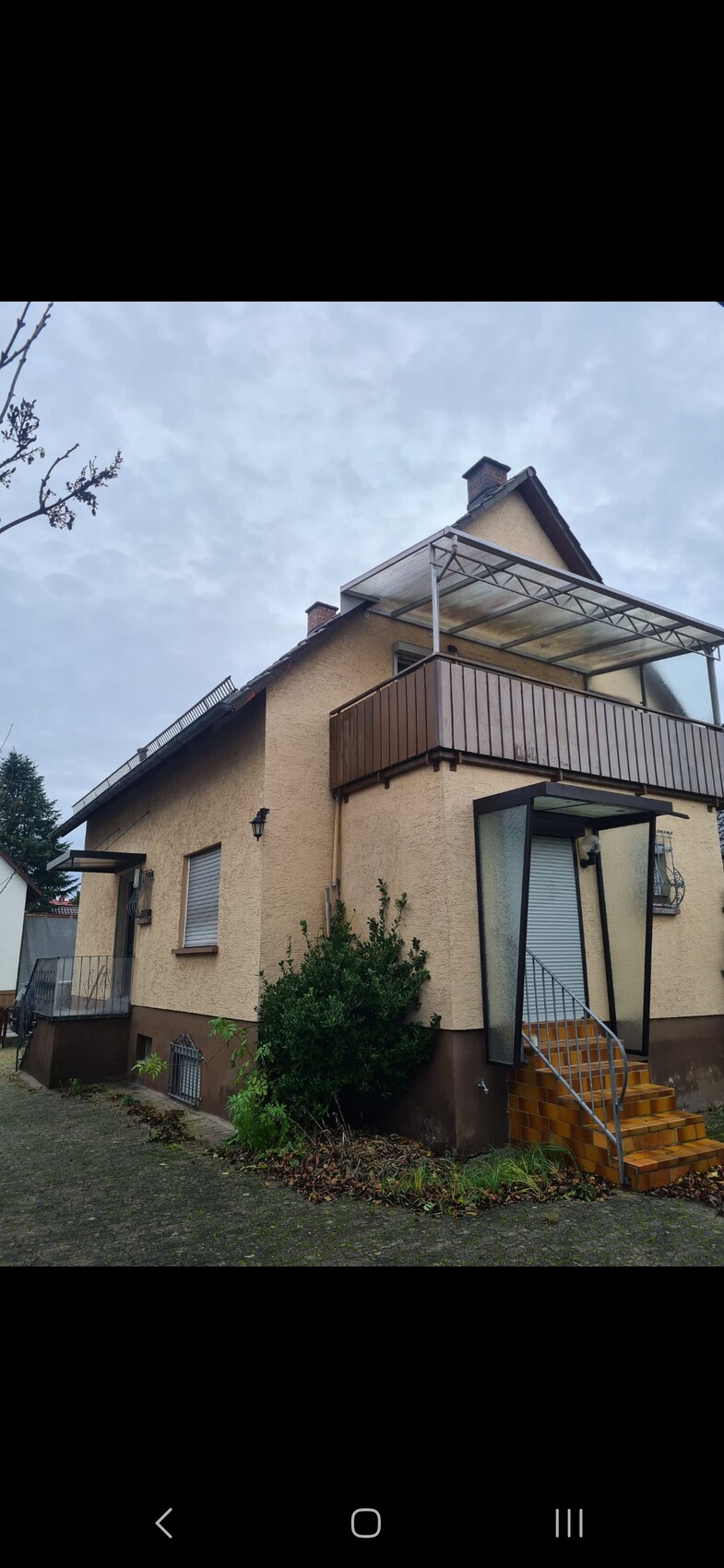 Zweistöckiges beiges Haus mit Balkon, Vordach und Treppe mit orangefarbenen Fliesen