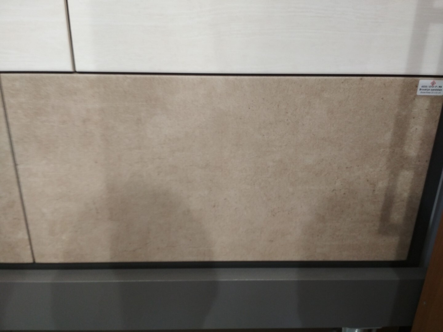 Beige Wandpaneel mit dunkler Sockel-Leiste und kleinem Aufkleber rechts oben.