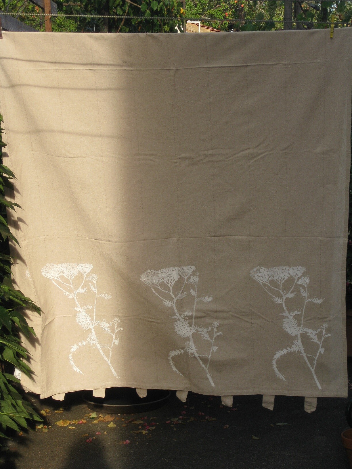 Beiger Stoffvorhang mit weißen Blumenmotiven im Gartenbereich aufgehängt