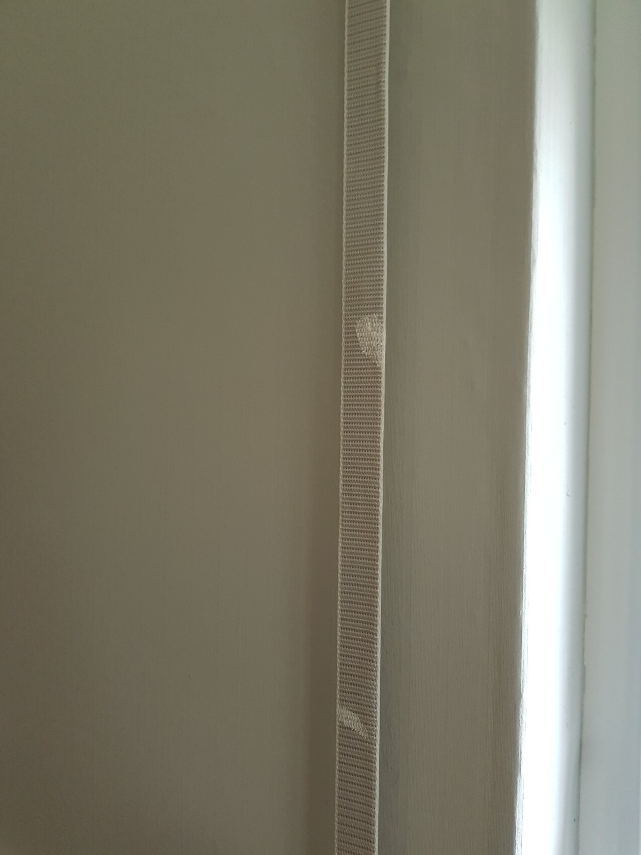 Beiges, vertikales Textilband an einer Tür-/Fensterleiste vor einer hellen Wand.