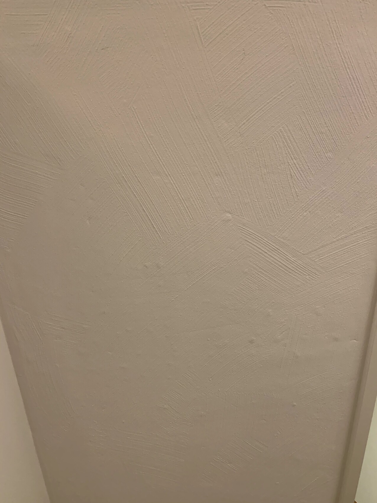Nahaufnahme einer hellbeigen Wand mit grober Putzstruktur und diagonalen Schraffuren.