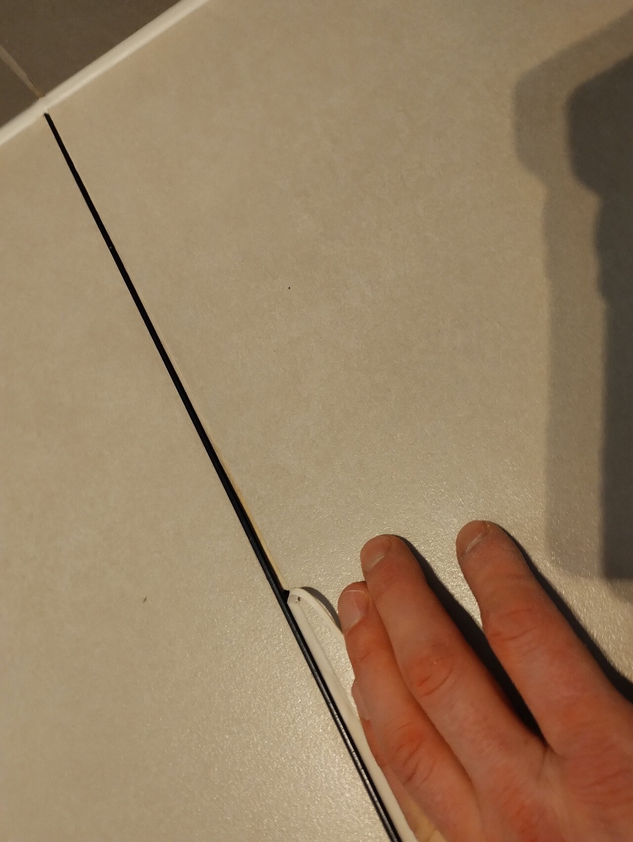 Beiger Fliesenboden, Hand berührt weißes Element am Rand der Fläche