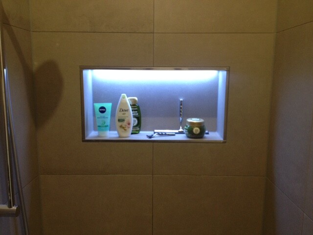 Beleuchtete Duschnische in Fliesenwand mit Shampoo, Duschgel, Creme und Rasierer.