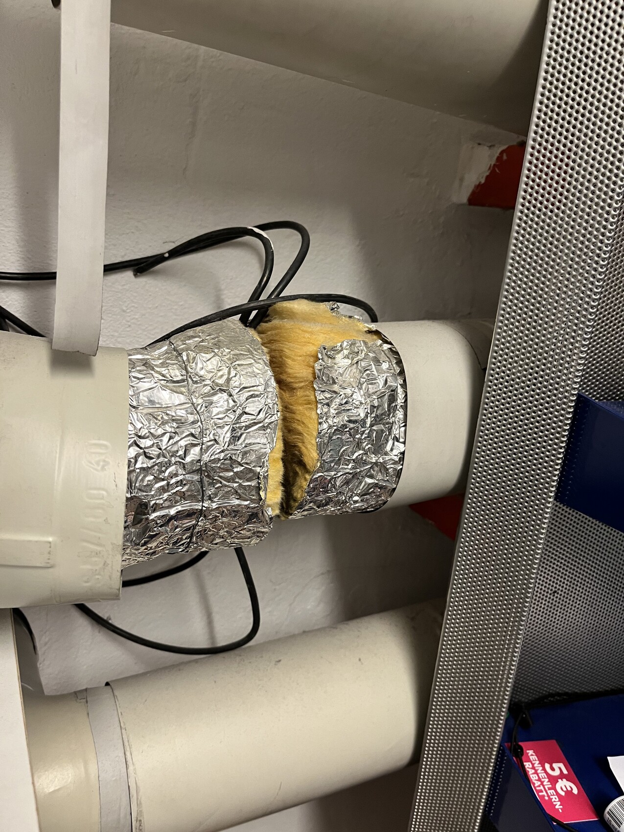 Isoliertes Rohr mit gelber Dämmung, umhüllt von Aluminiumfolie, Kabel daneben.