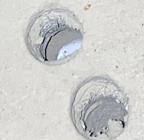 Zwei kreisförmige Bohrlöcher in rauem Beton, Ränder abgebrochen, Innenseite sichtbar.