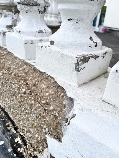 Weiße Balustrade mit abgeplatztem Putz und freigelegtem Untergrund im Außenbereich.