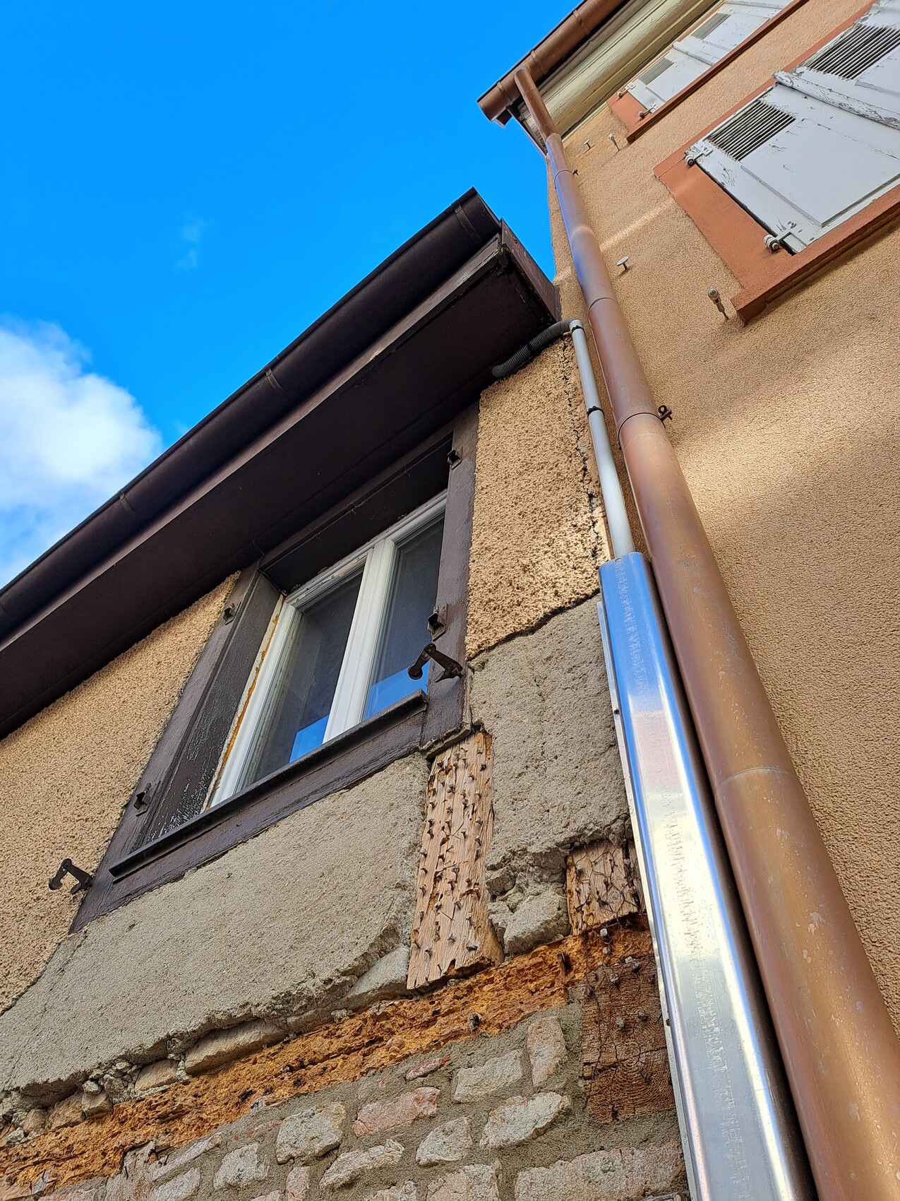 Außenansicht eines beschädigten Hauses: bröckelnder Putz, freiliegende Mauer, Fenster, Regenrinne