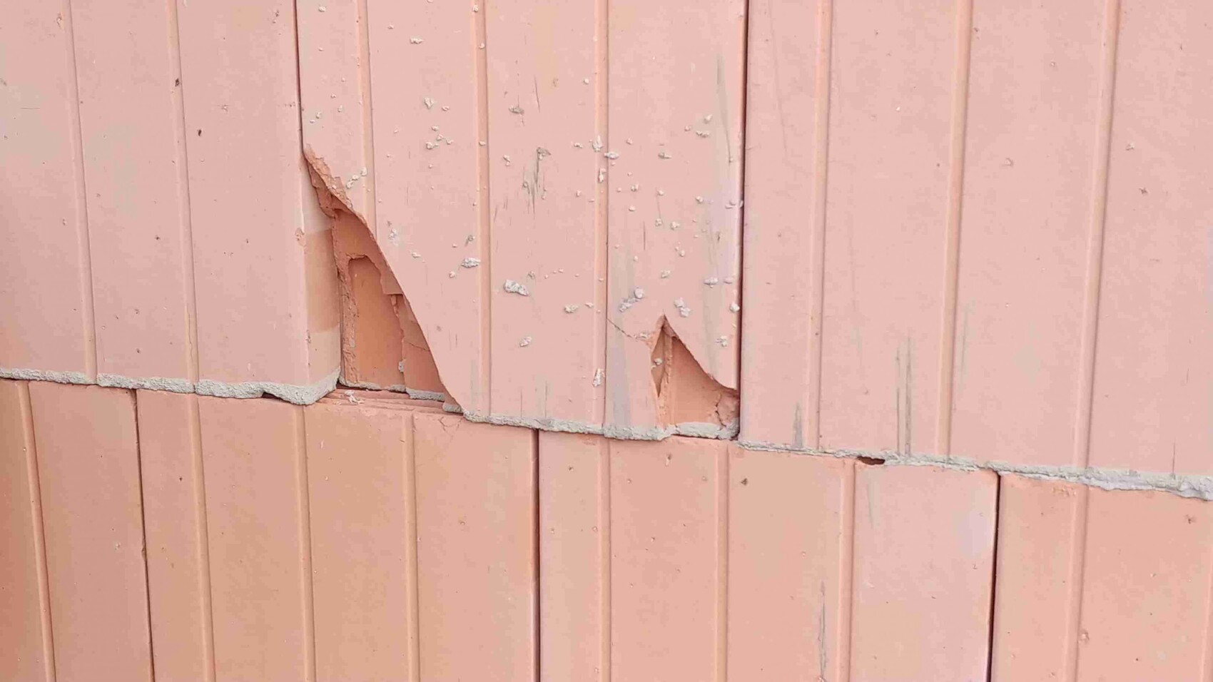 Aussenwandverkleidung mit beschädigten pinkfarbenen Paneele, Rissen und Abplatzungen