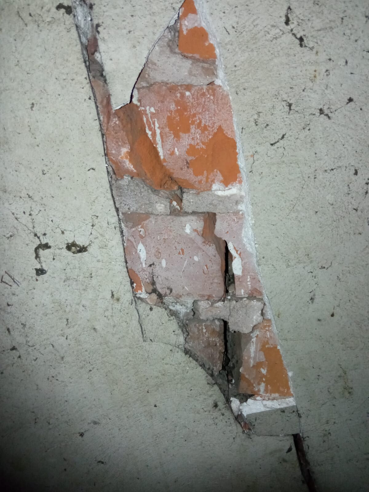 Riss in einer Wand mit freigelegten roten Ziegeln und bröckeligem Putz.