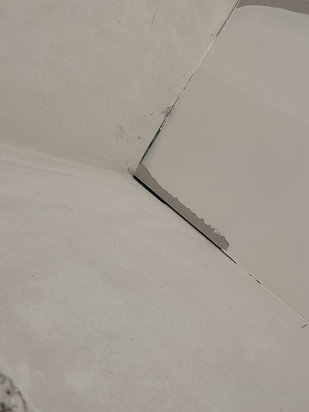 Schräg aufgenommenes Eckstück zwischen Wand und Boden mit Riss und Abplatzung.