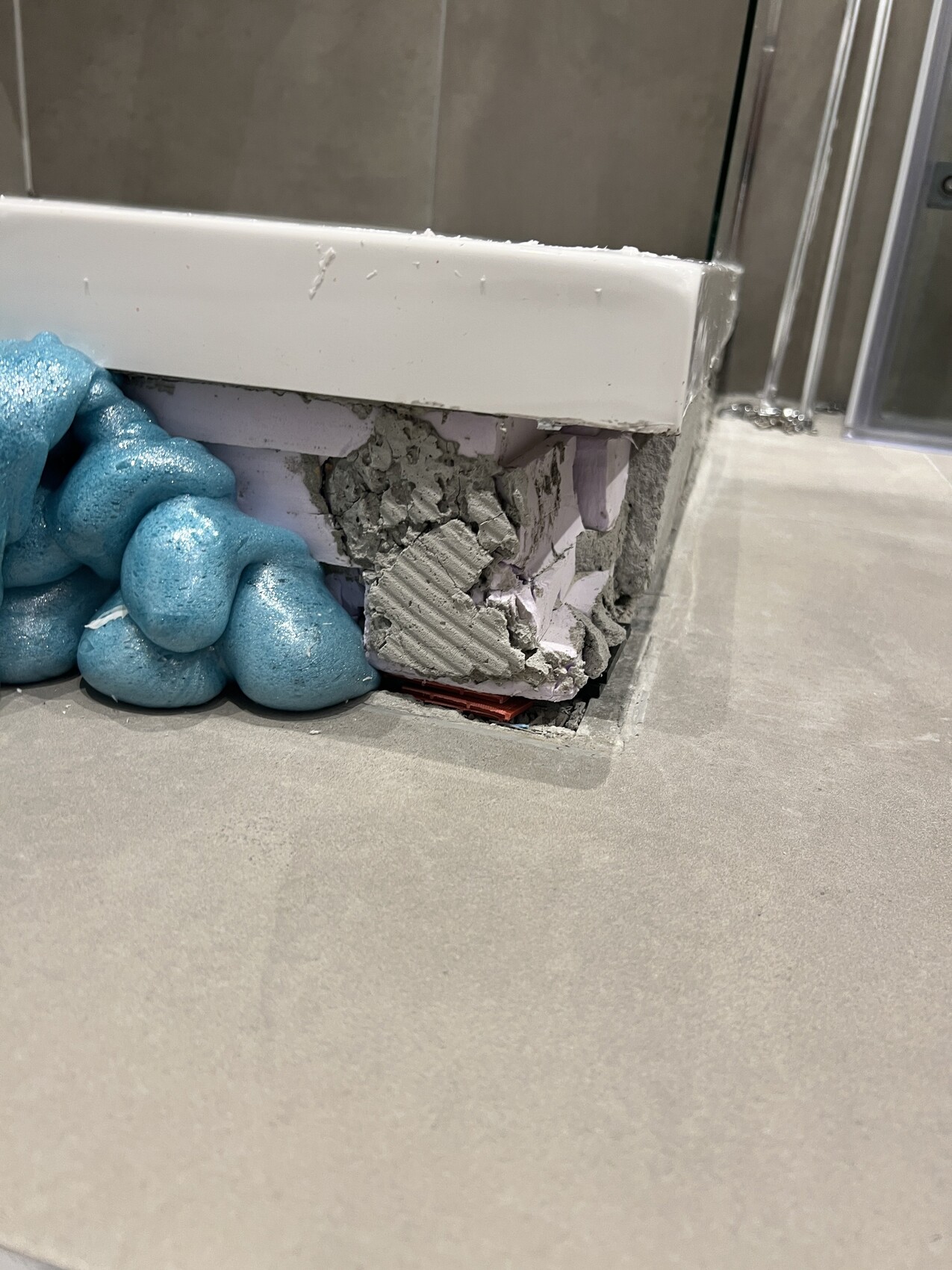 Offene Wandkante im Badezimmer mit Zementbruch, blaue Montageschaumklumpen daneben.