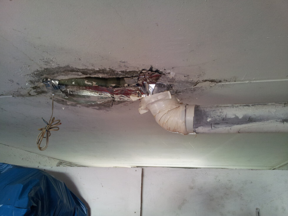 Beschädigte Decke mit offenem Rohrdurchbruch, Dichtband und Kabel auf Baustelle