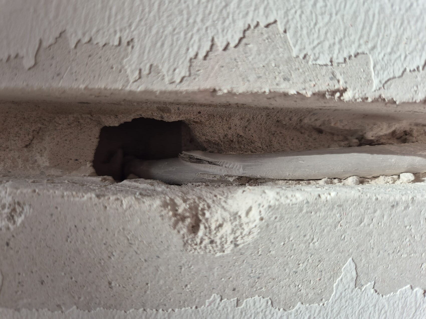 Rissige verputzte Wand mit Spalt, durch den ein rohrähnlicher Kanal sichtbar ist, staubig.