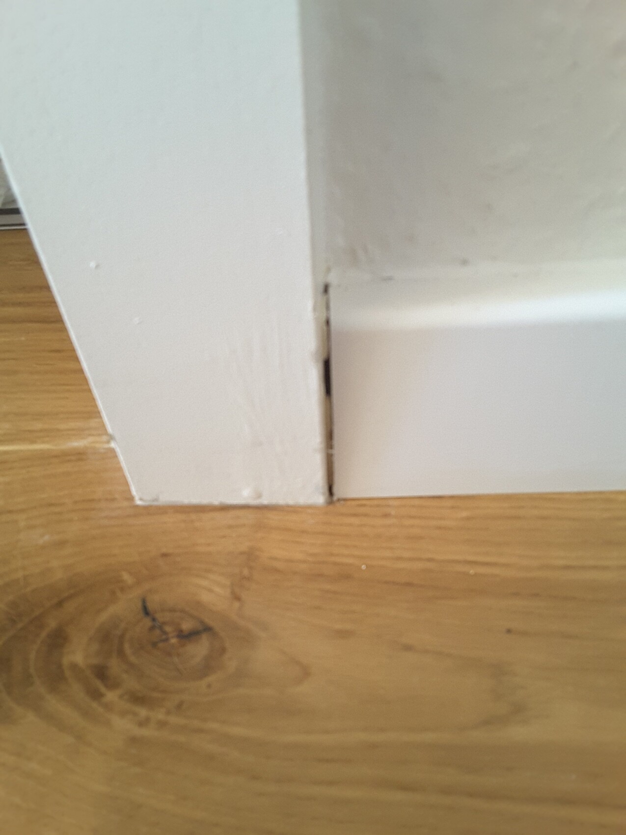 Weißer Sockelbereich an Wand-Ecke mit Spalt zwischen Sockel und Wand über Holzboden.