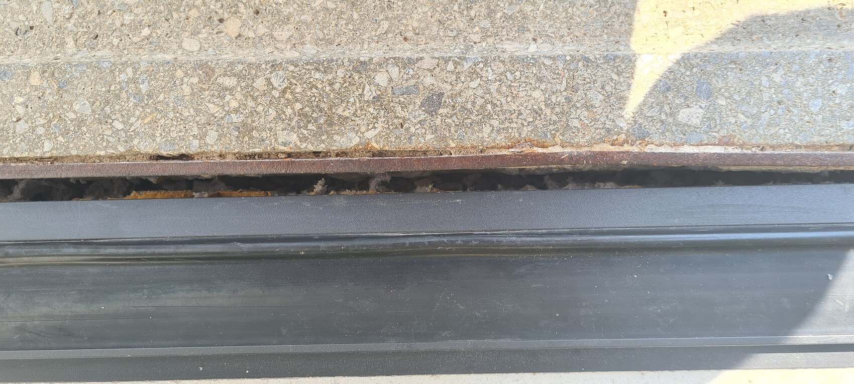 Sichtbarer Betonstufenabsatz mit rostiger Kante, darunter dunkle Fuge und schwarze Türschwelle.