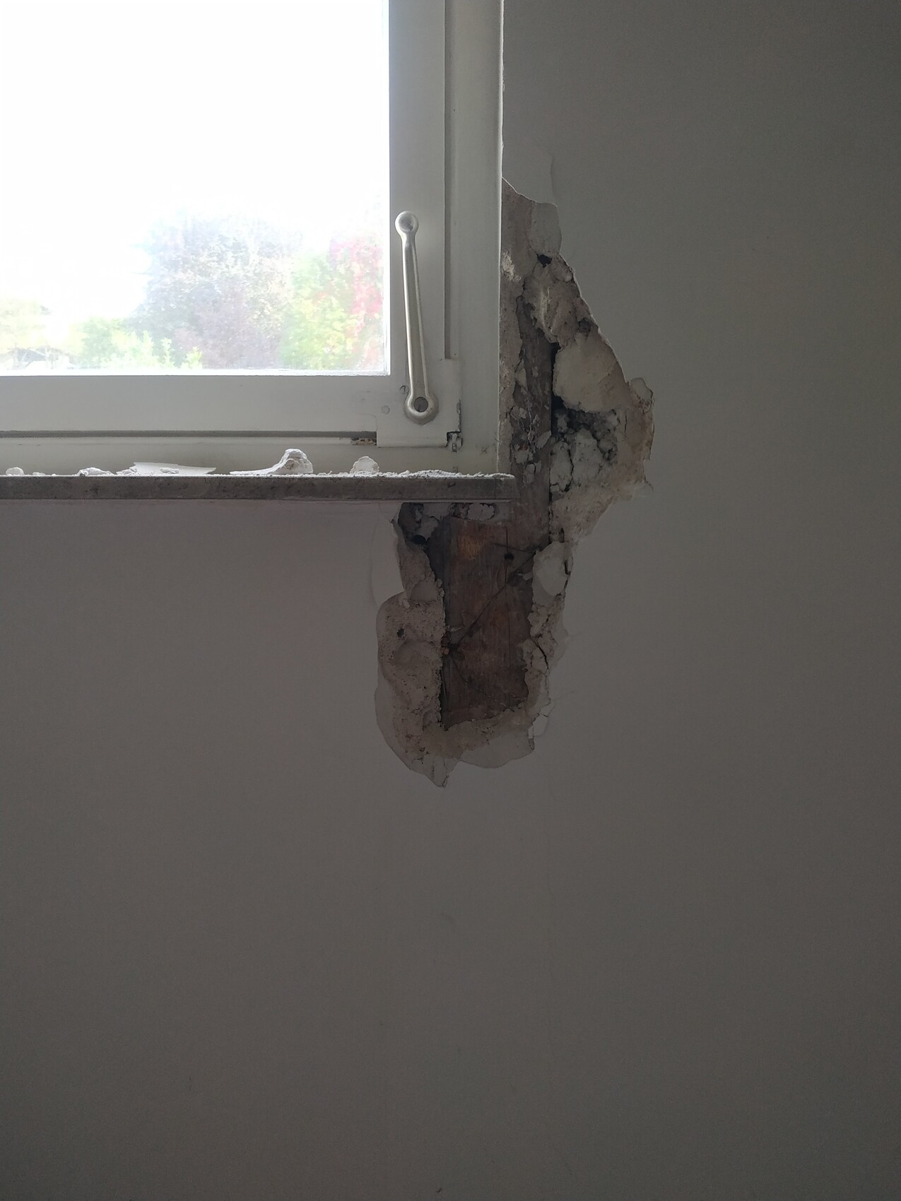 Fensterrahmen in einer beschädigten Wand, bröckelnder Putz und freiliegendes Mauerwerk.