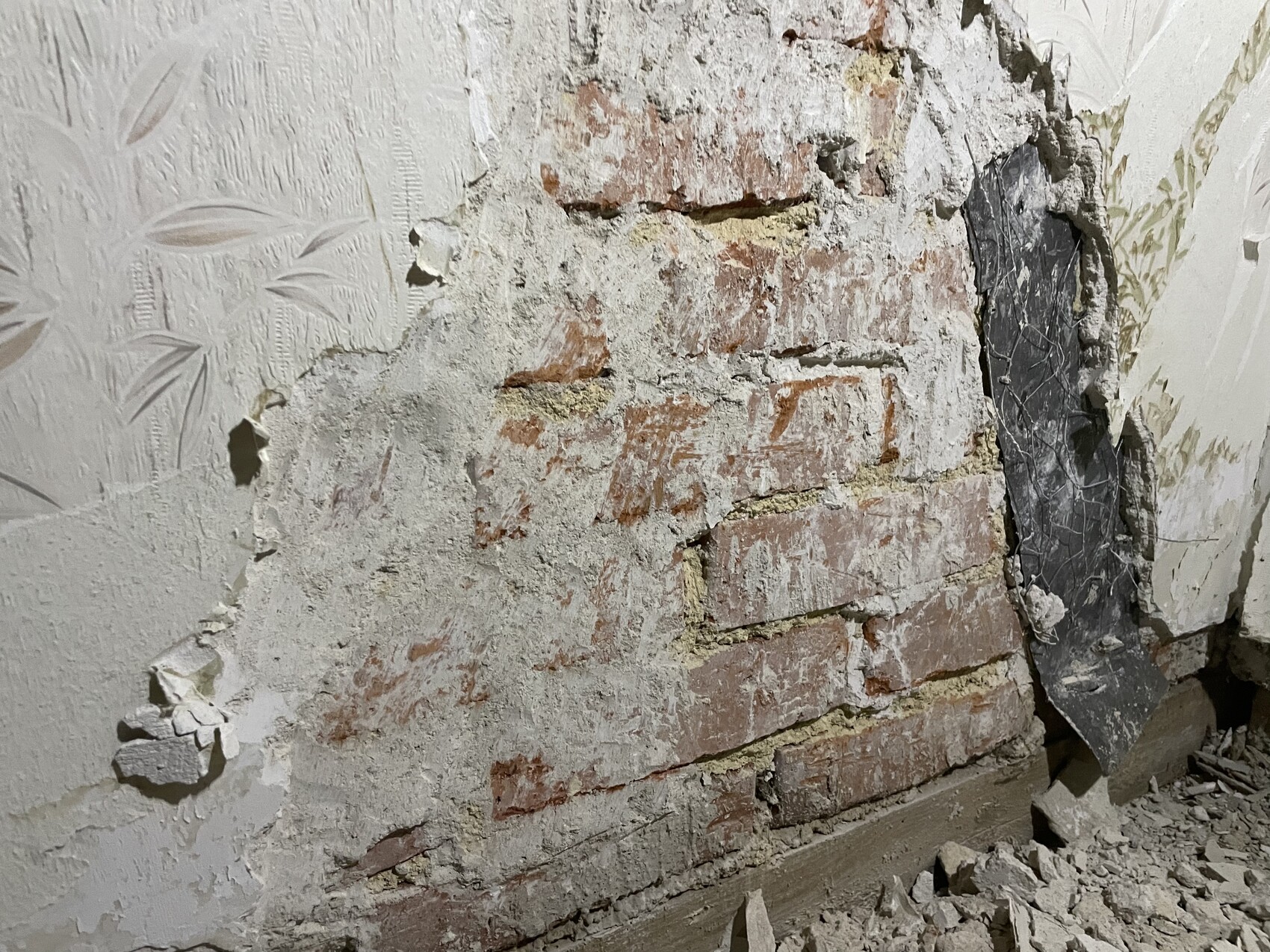 Zerfallene Innenwand mit freigelegtem Backstein, bröckeligem Putz und Staubtrümmern.