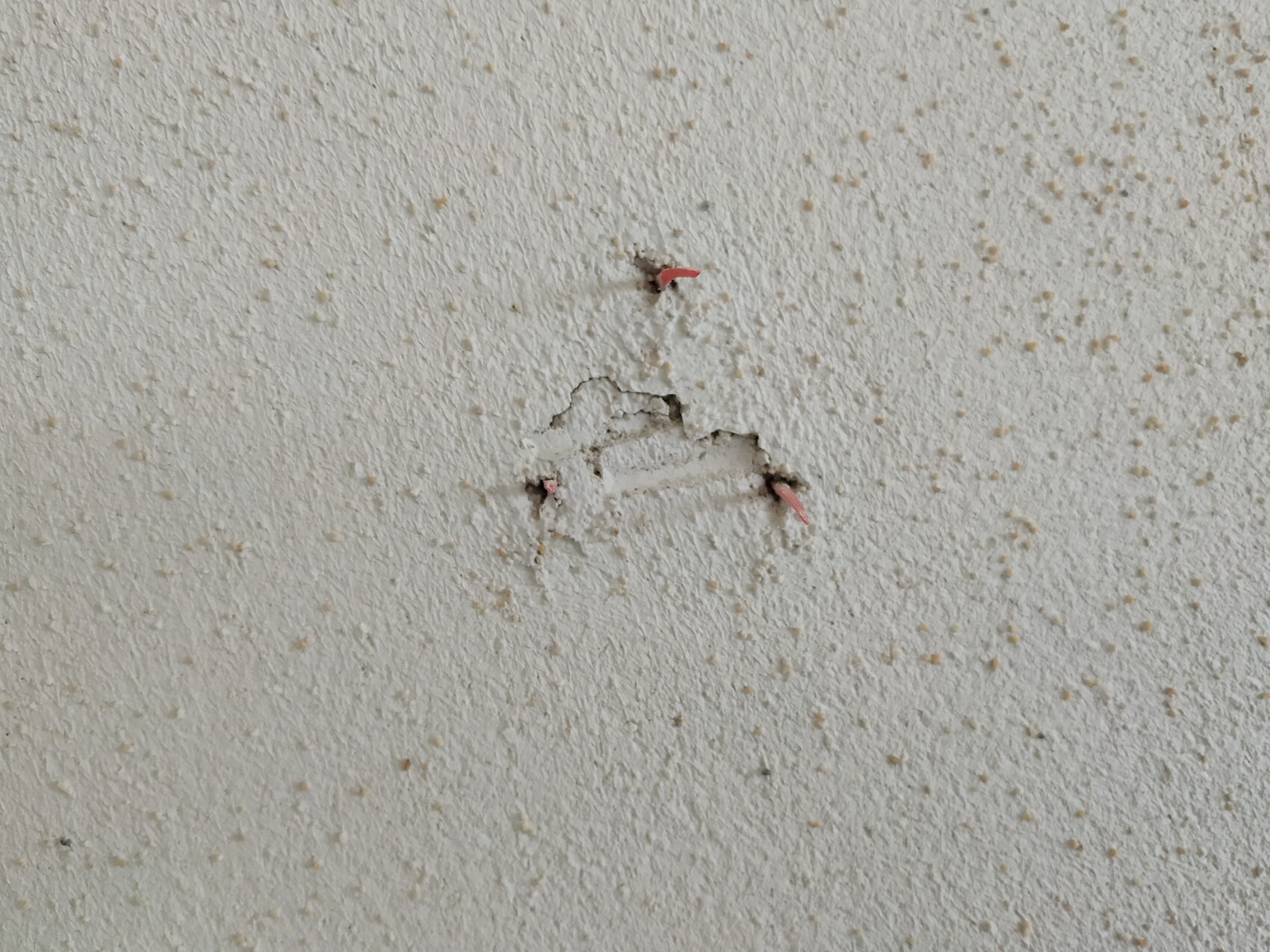 Weiße, strukturierte Wand mit kleinem Loch und freiliegten roten Drahtfäden.