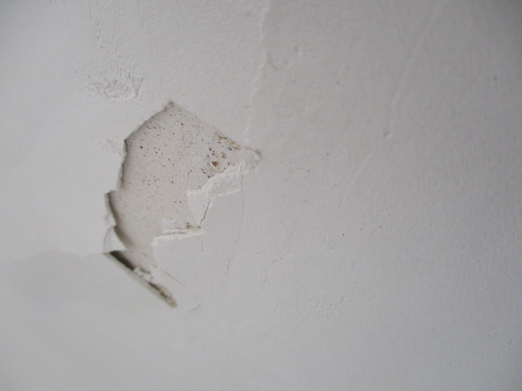 Weiße Wand mit Loch im Putz, sichtbares inneres Material und Risse.