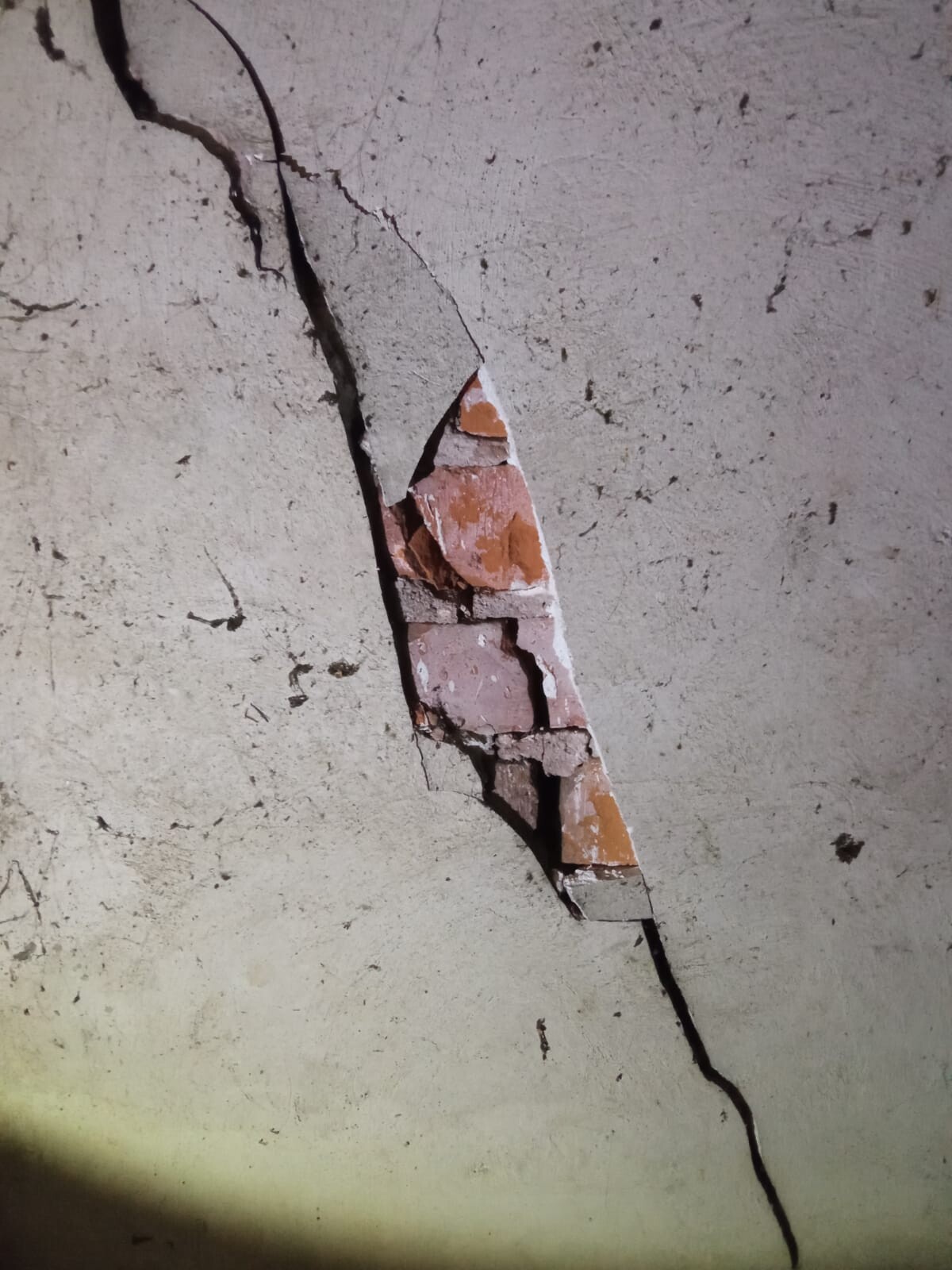 Diagonaler Riss in der Wand mit freiliegenden orangefarbenen Ziegeln hinter bröckelndem Putz.