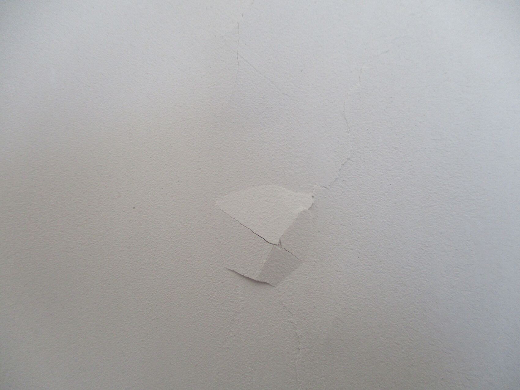 Weiße Wand mit einem Riss und abblätterndem Putz in der Mitte.