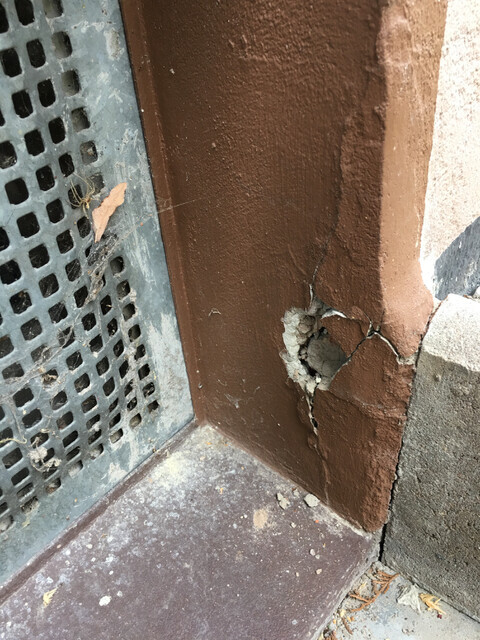 Nahaufnahme von beschädigter Wand mit Rissen und abplatzendem Putz neben Metallgitter