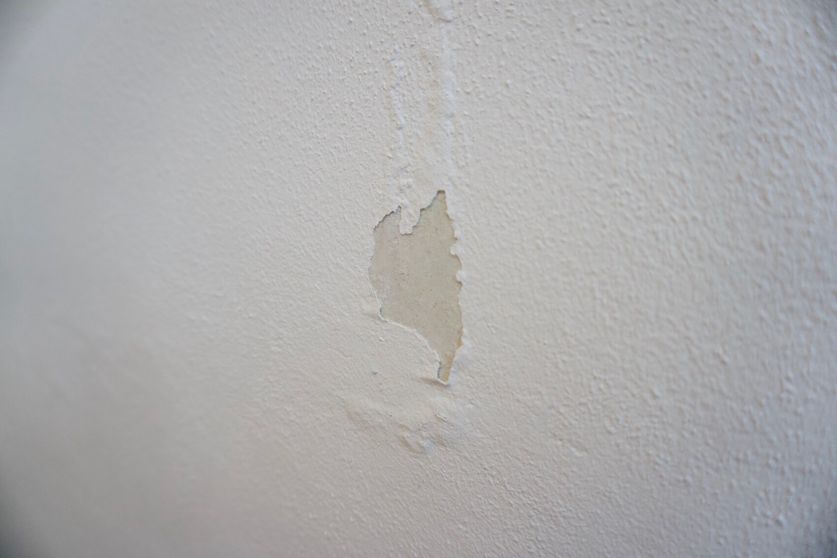 Weiße Wand mit einer abblätternden Putzstelle in der Mitte.